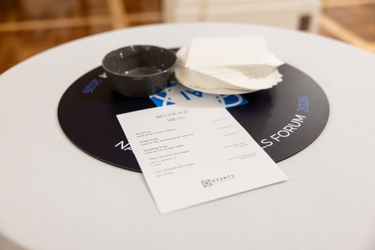 A cocktail table at the evening function, with a branded forum table disk, a printed beverage menu and napkins.
