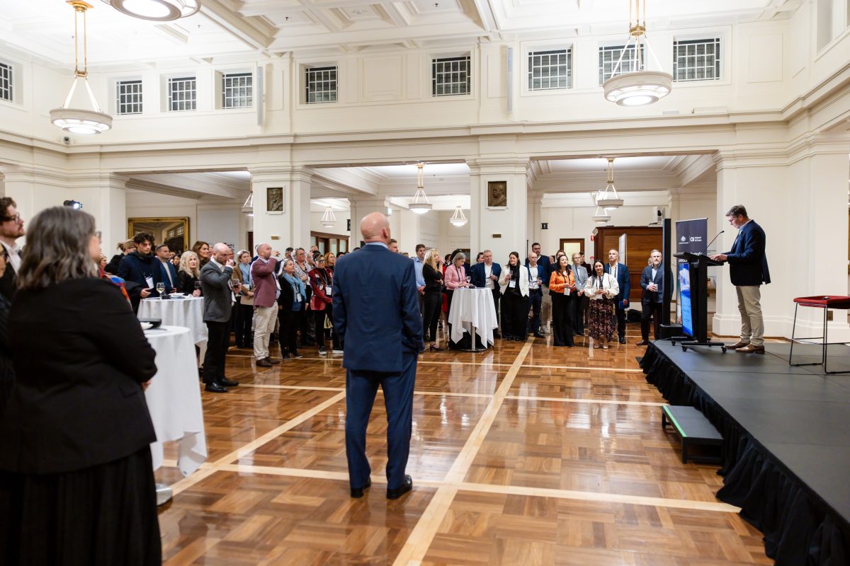 King’s Hall during the evening function, guests gathered on the parquet floor around cocktail tables while a speaker addresses the room from a low stage.