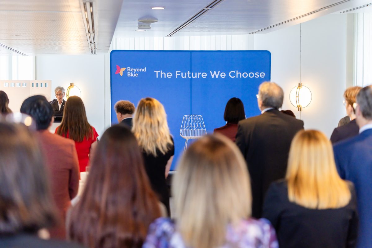 • Audience wide: The launch under way in the Dame Enid Lyons Alcove, guests standing through the room while a speaker addresses them from the branded lectern, with the event backdrop behind.