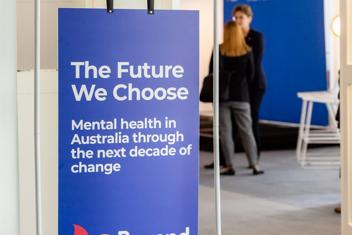 • Blue sign with guest passing: The blue version of The Future We Choose signage standing in the alcove as a guest walks by, with the event backdrop behind.
