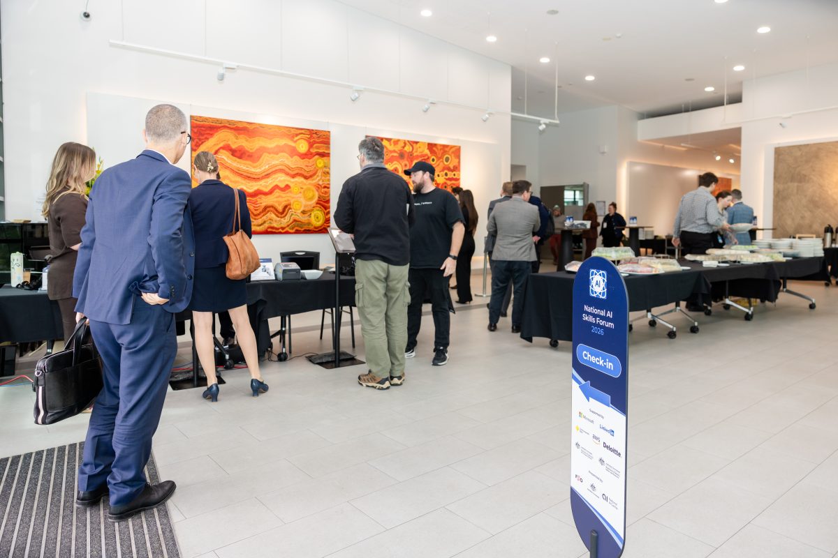 Guests arriving at the Ann Harding Conference Centre foyer, with the check-in desk and catering tables set up beneath large Aboriginal paintings and a Check-in wayfinder sign in the foreground.