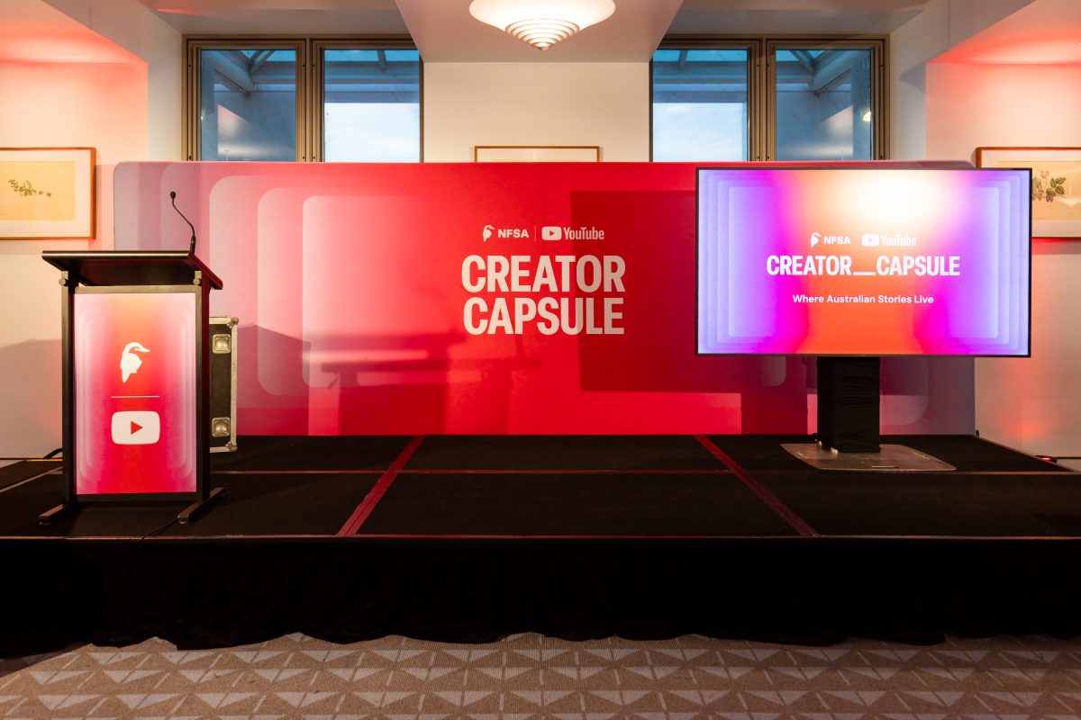 • The Creator Capsule stage at Parliament House, with a red NFSA and YouTube backdrop wall, an illuminated lectern and a screen, flanked by branded flight cases.