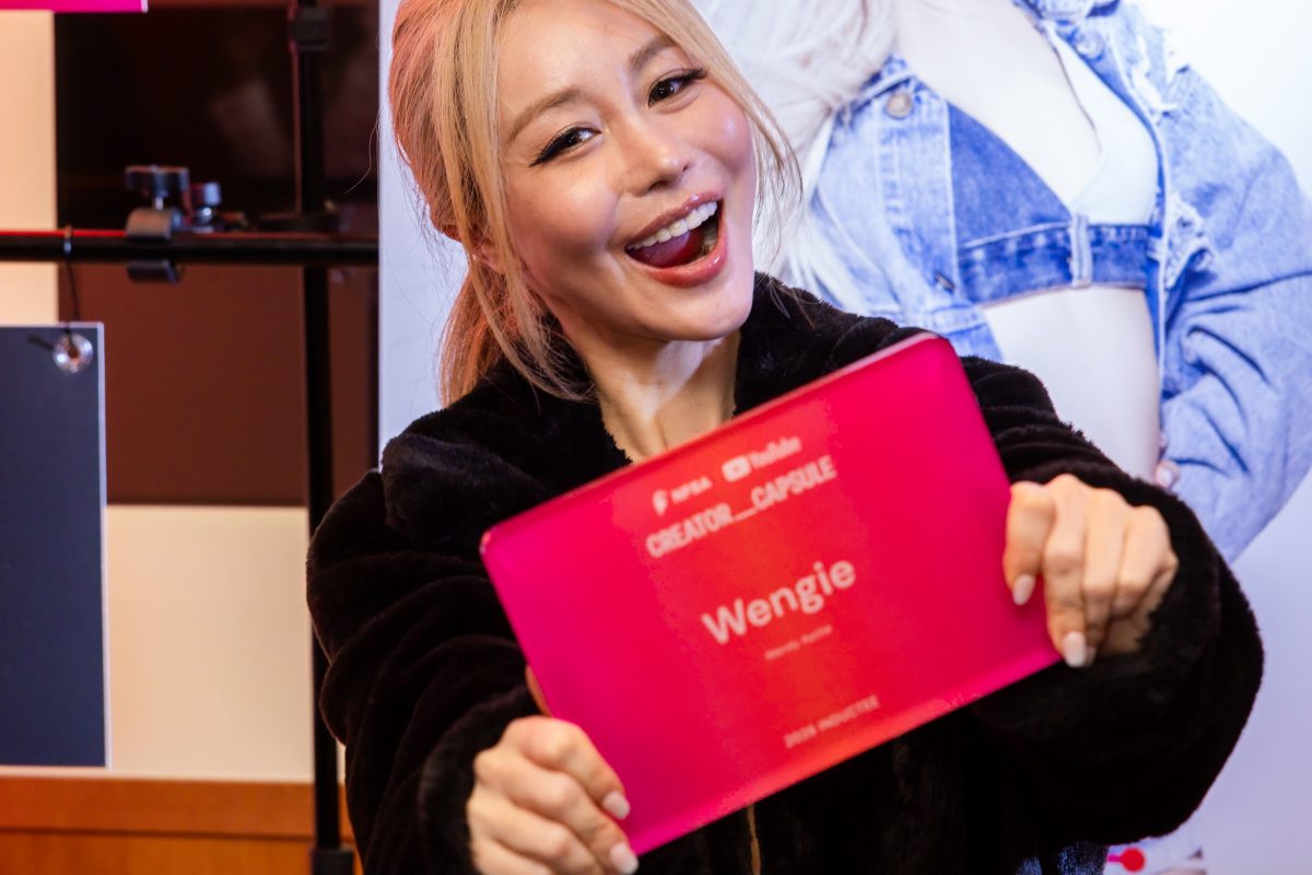YouTube creator Wengie holding her pink Creator Capsule inductee plaque, smiling in front of her own display portrait at the Parliament House launch.