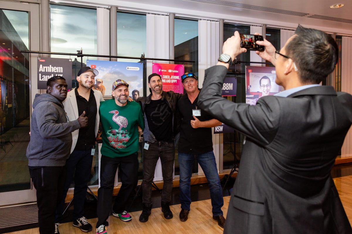 • Creator stations at the Creator Capsule launch, lit in magenta and red, with hanging panels showing a creator portrait, channel statistics and a written biography on freestanding rigs set in front of the room’s existing framed artworks.