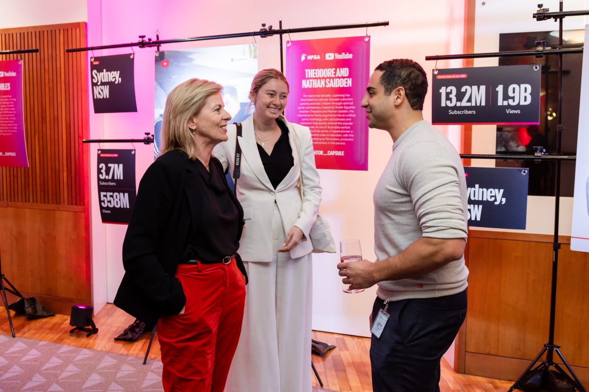 • Creator stations at the Creator Capsule launch, lit in magenta and red, with hanging panels showing a creator portrait, channel statistics and a written biography on freestanding rigs set in front of the room’s existing framed artworks.