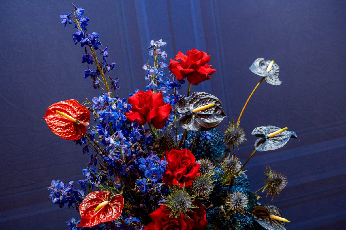 Red roses, anthuriums, blue delphinium and sea holly arranged against a navy panelled backdrop for the Netflix The Diplomat Season 4 launch