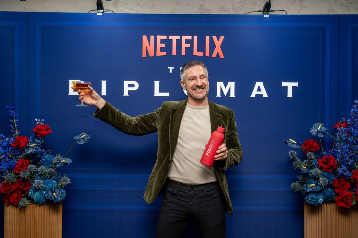 Red POLITICO water bottle with a Diplomat cocktail Custom Netflix The Diplomat media wall in deep navy with raised lettering and florals, flanked by neon cinema numbers at Palace Electric Cinema NewActon