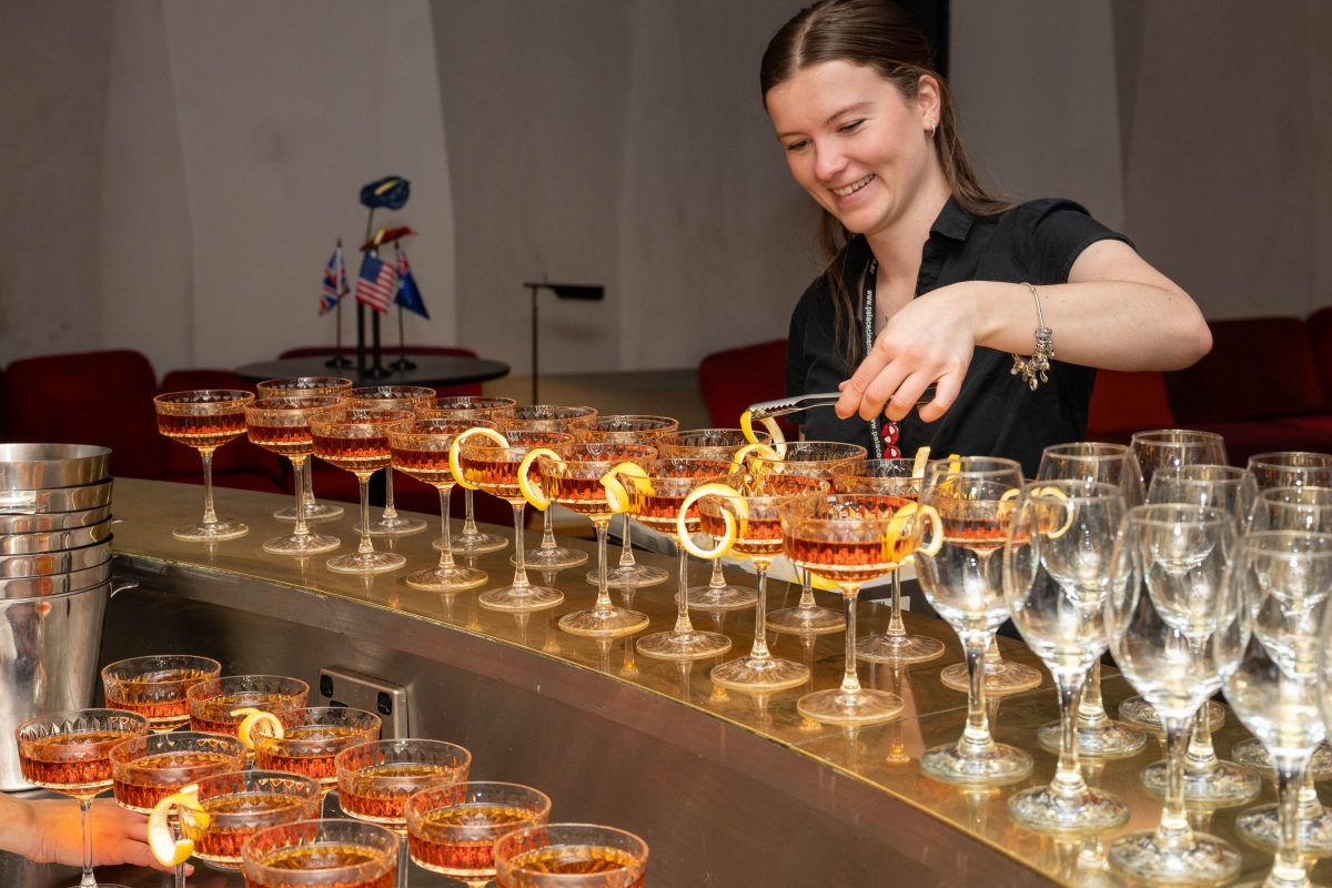 Bartender garnishing rows of Diplomat cocktails in cut crystal coupes with lemon twists at a Canberra launch event